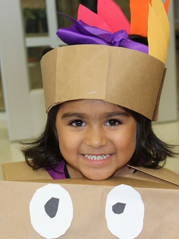 Student wears a turkey headdress and smiles 